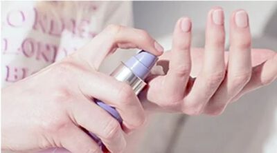 A hand holding a purple pump bottle, dispensing a cream onto a fingertip.