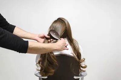 A person is brushing long hair of another person, who is seated and facing away.