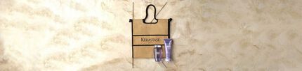 A woven tote bag with the logo "Kerastase" displayed against a textured beige background, accompanied by two hair care products.