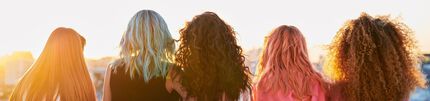 Five individuals stand side by side, facing away from the camera, showcasing a variety of long hairstyles in a sunset setting.