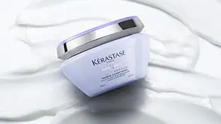 A Kerastase hair care product jar is placed on a smooth, creamy background, emphasizing its sleek design and branding.