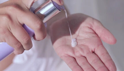 A hand holding a bottle is dispensing a small amount of creamy liquid onto an open palm.