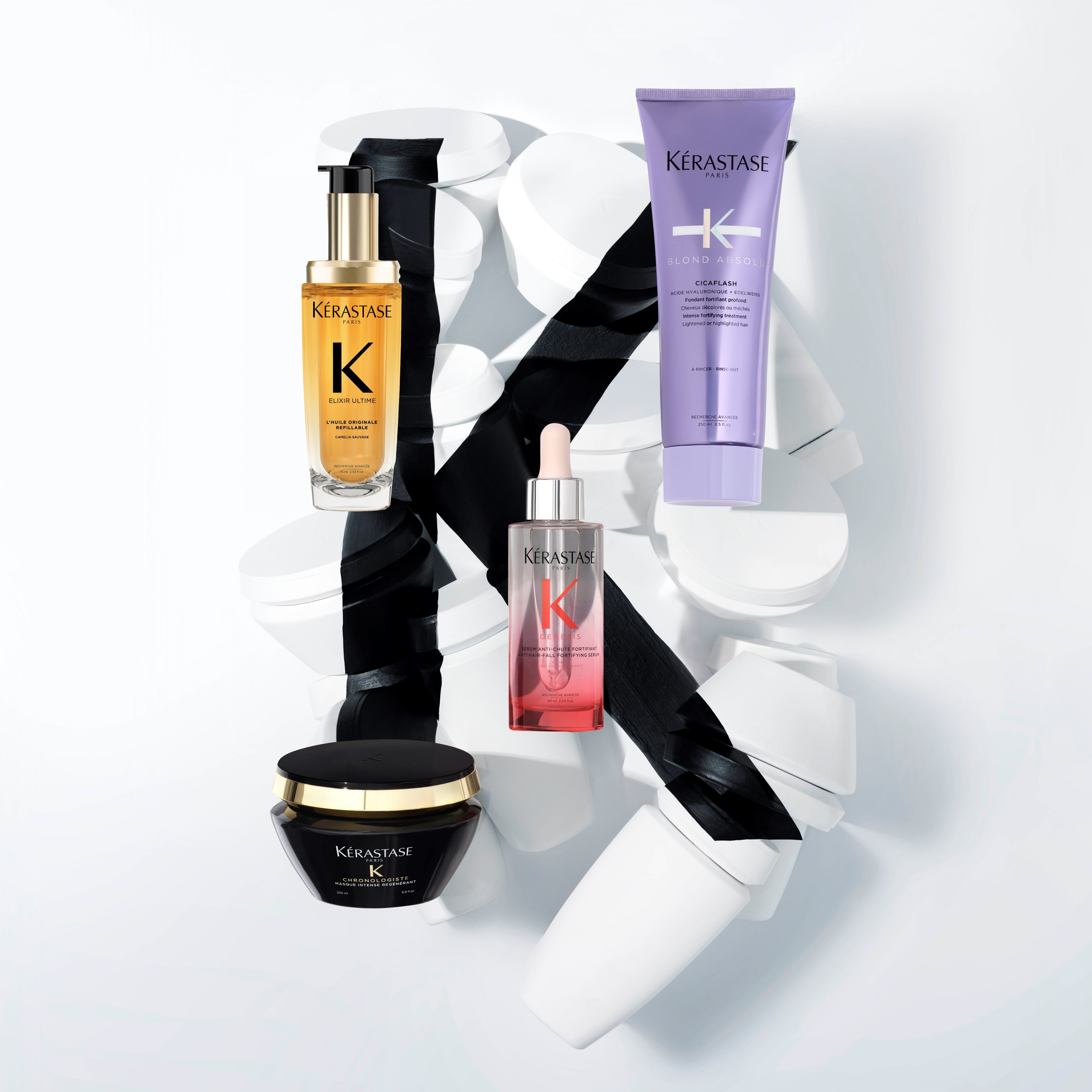 Four Kerastase hair care products artistically arranged on white containers, accentuated with a black ribbon backdrop.
