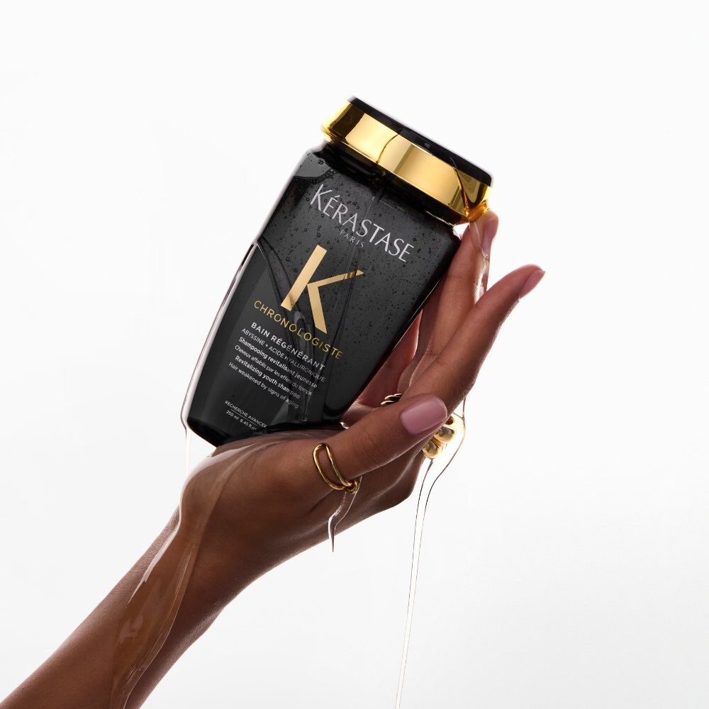 A woman’s hand holds Chronologiste Bain Regenerant Shampoo, an anti- ageing haircare shampoo.