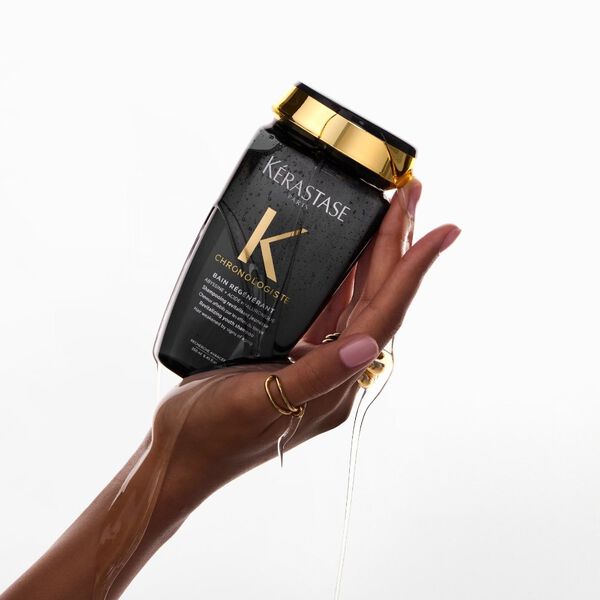 A woman’s hand holds Chronologiste Bain Regenerant Shampoo, an anti- ageing haircare shampoo.