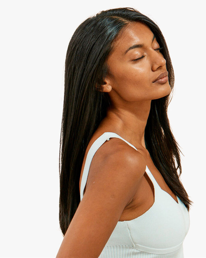 A young woman with long, straight hair is gazing upwards with her eyes closed, wearing a light blue tank top.