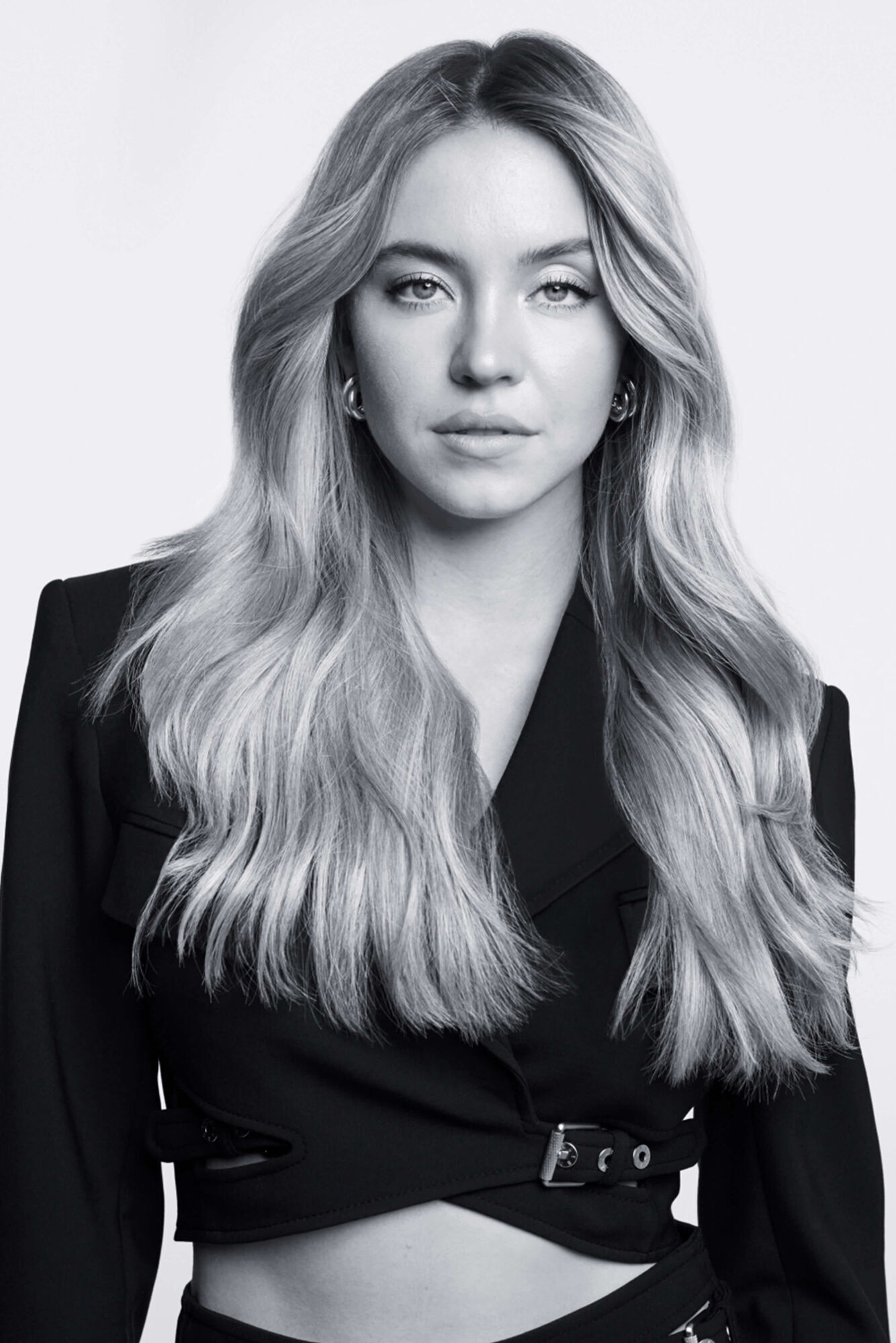 A monochrome portrait of a young woman with long, wavy hair, wearing a stylish black jacket. She has a serious expression and is facing the camera.