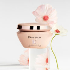 Kerastase Gloss Absolu hair mask propped on top of clear blocks with a grey background and flowers​​