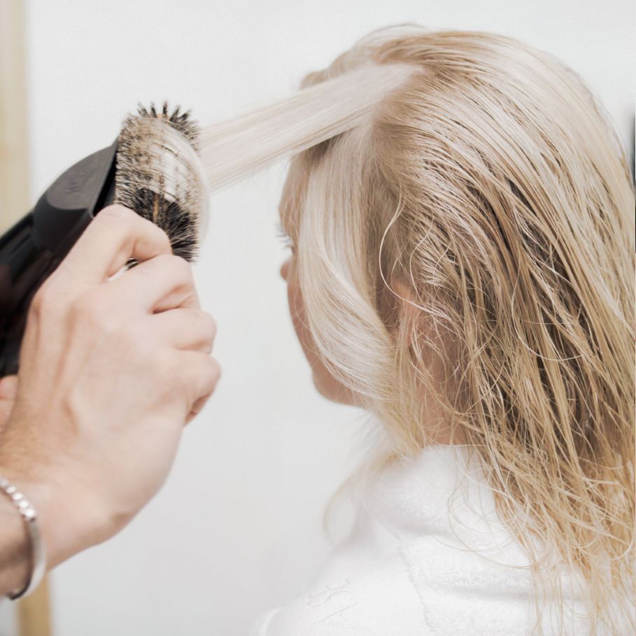 Person using blow dryer and brush to style hair demonstrating heat styling techniques that can cause hair breakage without proper heat protection