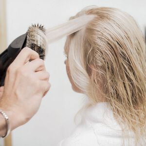 Person using blow dryer and brush to style hair demonstrating heat styling techniques that can cause hair breakage without proper heat protection