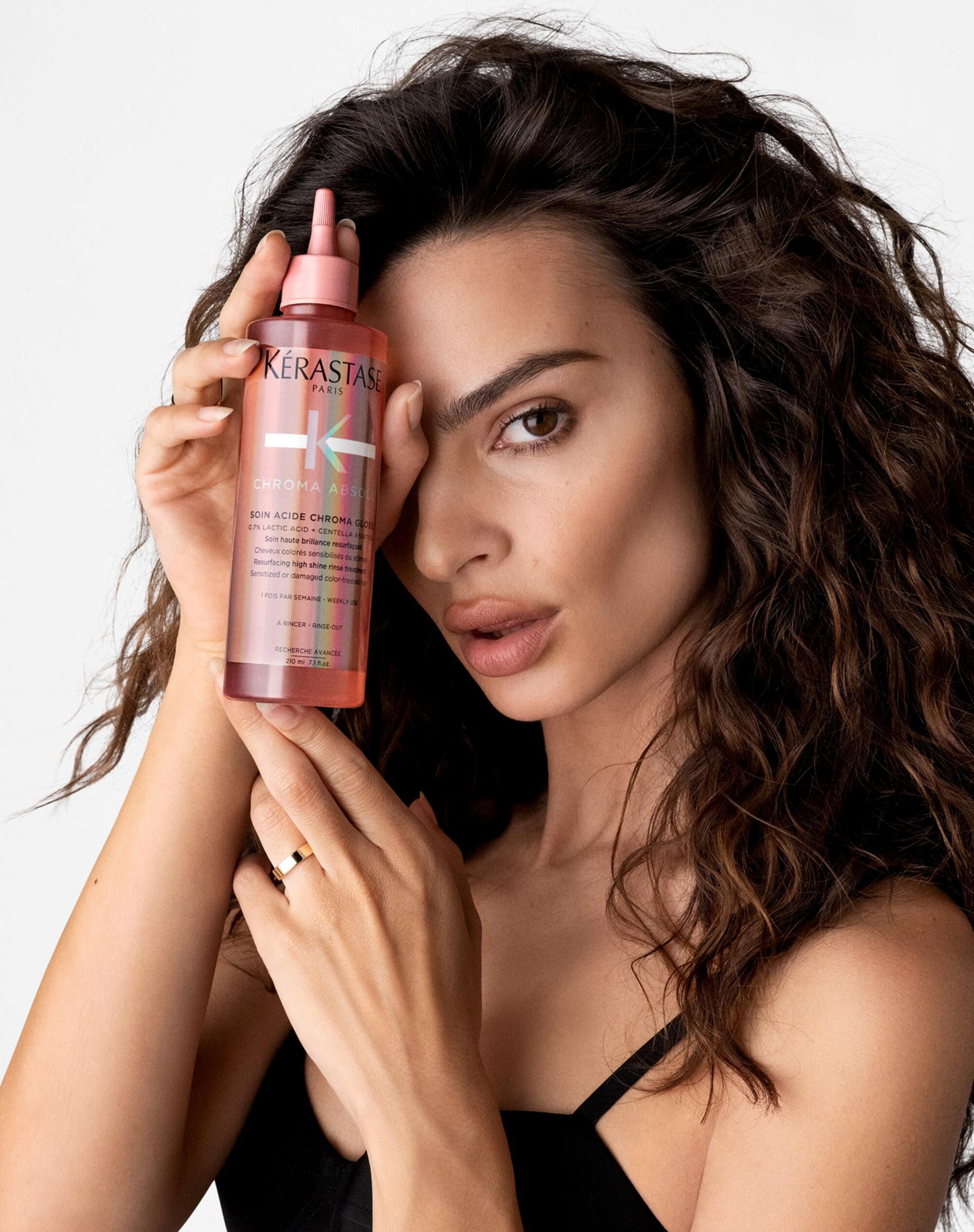 Emily Ratajkowski holding a pink bottle in front of her right eye.