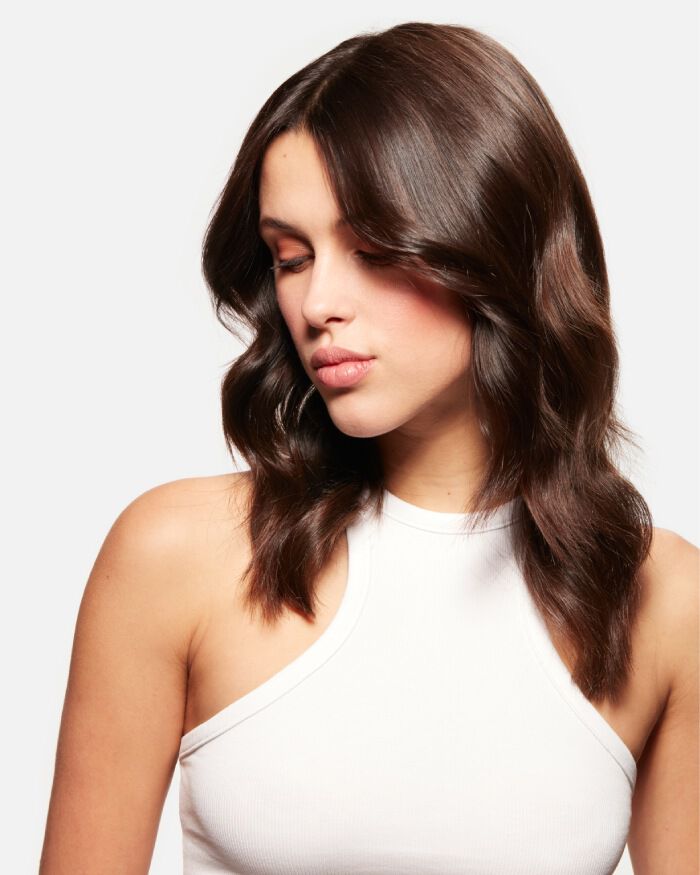 A woman with long, wavy brown hair is looking to the side, wearing a sleeveless white top. Her expression is thoughtful and serene.