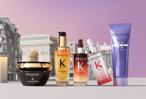 A selection of Kerastase hair care products displayed in front of a stylized background featuring architectural elements. The products include a black jar, various serums, and a purple tube, all prominently labeled with the Kerastase logo.
