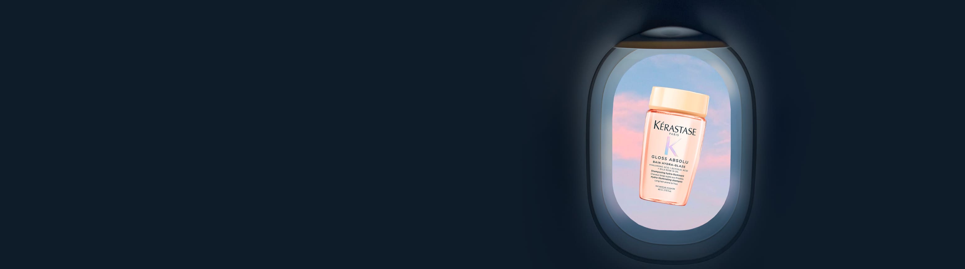 A travel-sized translucent pink bottle of Kérastase Gloss Absolu Bain Hydra-Glaze, floating in the center of an airplane window, with a pastel pink and blue sky.