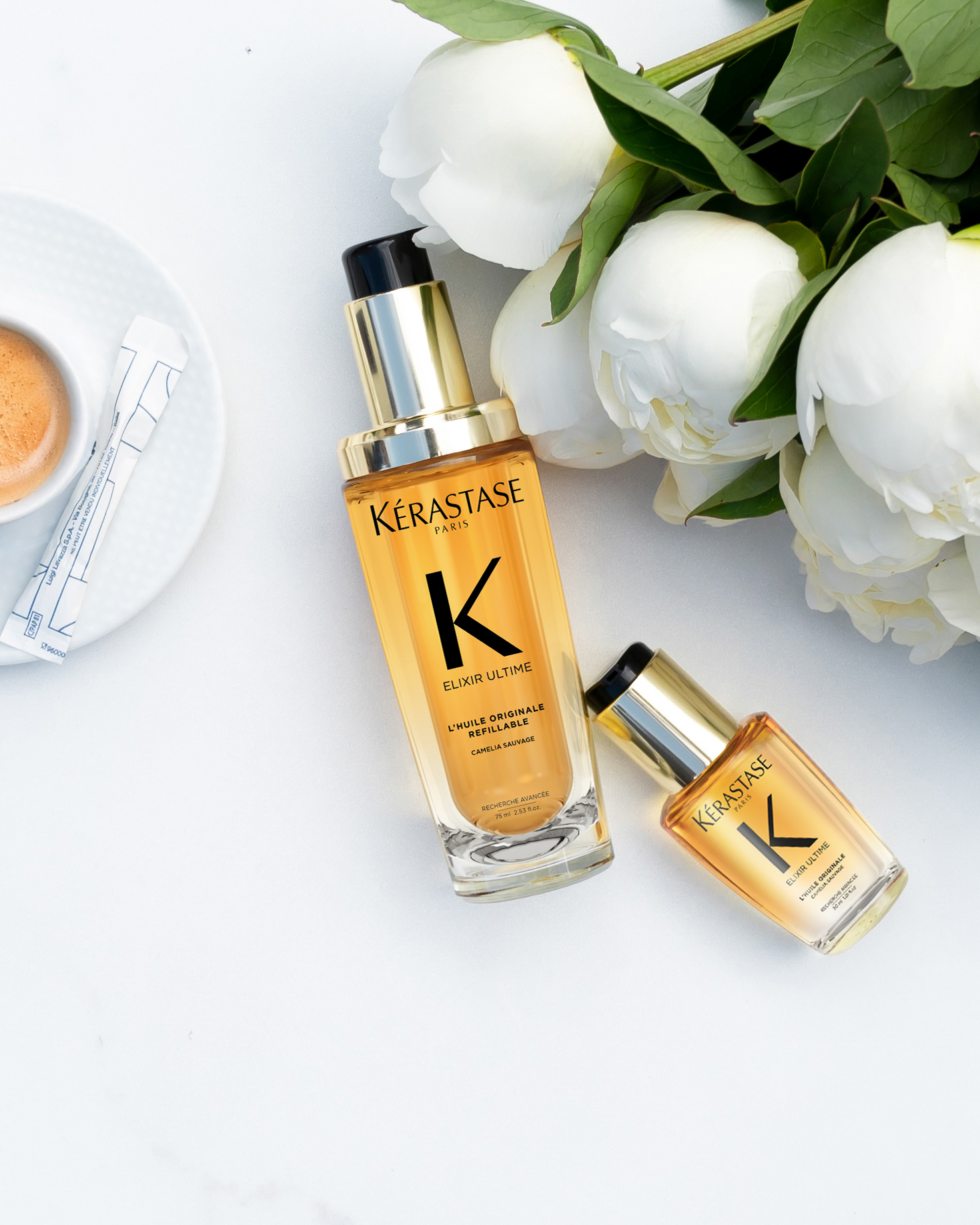 Full size and travel size Elixir Ultime Huile Originale on a white table with coffee and white flowers
