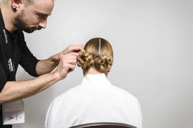 A hairstylist carefully styles a client's hair into two elegant buns, showcasing a professional hairdressing setting.