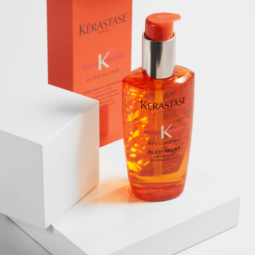 Discipline Oleo Relax hair oil is set on a simple white platforme in a pure grey background while its bright orange color sparkles.