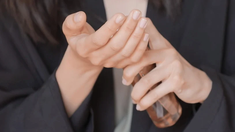 Using Your Hands to Style Your Hair With Kerastase Elixir Ultime Hair Oils A close-up of a person's hands applying a fragrance from a glass spray bottle.