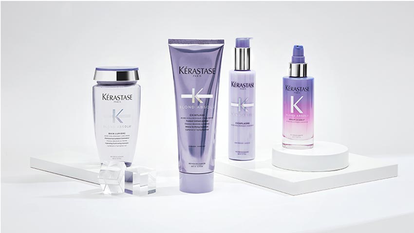 Four Kerastase hair care products displayed on white pedestals, featuring sleek packaging in purple and silver tones.
