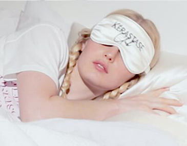 A woman with braids wearing a silk sleep mask rests peacefully on a pillow, promoting relaxation and self-care.